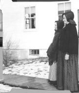 SA0184 - Eldress Lizzie and Sister Prudence are shown outside a building, standing on a wooden walkway; snow I on the ground. Identified on the back. See comment field for SA 0198.